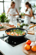 © ZaStock - Fresh vegetables sizzle in a skillet as friends explore healthy cooking together in a modern kitchen. Laughter and vibrant ingredients create a joyful atmosphere for collaboration
