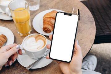 Mockup woman's hand holding using smart phone with white blank screen POV at coffee shop, mobile app design and advertising, online marketing