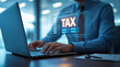 © MDGOLAM - A futuristic holographic interface on a laptop displays 'TAX' and completed tasks, showcasing advanced tax management in a modern office setting, promoting professionalism and efficiency.