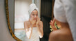 © Raushan_films - Indian young adult gen z woman lady teen girl female wrapped towel on head and body look mirror use fresh foam soap apply wet dry cheek take sink water hand splash on face do self skin care day home