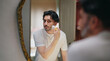 © Raushan_films - Indian Asian gen z young adult smiling guy bearded man look mirror hold soft brush apply white foam gel cream to his beard face before shave do morning day self skin care routine indoor house
