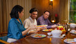 © Raushan_films - Indian family group sitting around dining table chair enjoy night dinner indoor home happy mom lady serve fresh salad cute kid boy dad hold spoon eat tasty food talk gossip have fun joy spend time