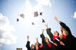 © deagreez - Jubilant graduates celebrating outdoors, tossing mortarboards into the sky, marking the completion of their academic journey on sunny day.
