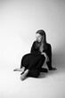 © Anhelina  - Black and white photo of young fantastic model. Studio. European type. White background. Emotional. Minimalist and stylish. Fashion shot of stylish vogue woman in black suit sitting on floor in studio