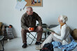 © pressmaster - Mature man with mug sitting by wall and looking at senior female refugee with open book during discussion of latest news