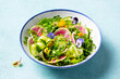 © annapustynnikova - Green salad with watermelon radish and edible flowers in a bowl. Blue background. Close up.