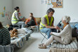 © pressmaster - Mature female volunteer in uniform holding hand of senior woman and comforting her while working in refugee camp