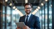 © Jasper - Confident Business Executive: A distinguished business professional stands in a modern office hallway, holding a digital tablet and wearing a suit and tie, conveying competence and professionalism
