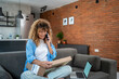 © Migma_Agency - Woman opening parcel at home and talking on mobile phone