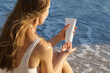 © Daryna  - Young woman applies cream on her fingers from a white mockup tube on the background of sea waves and sand. Concept of skin care, sunscreen, beauty products. Image for your design