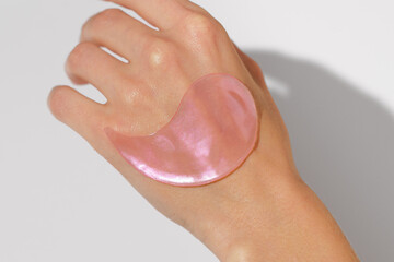 close-up of a pink hydrogel eye patch on female hand skin against a white background. hydrates, soot