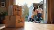© Eduardo Accorinti - Cardboard boxes labeled 'kitchen' and 'books' on hardwood floor in the foreground, with out of focus young couple carrying boxes and loading moving truck in the blurred background, moving to new home