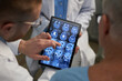 © DragonImages - Medical professionals analyzing detailed brain scans on tablet device screen during consultation session, showing close cooperation in diagnostic process