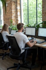 two people are sitting at a desk with multiple computer monitors. one of the people is typing on a k