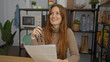 © Krakenimages.com - Woman smiling at desk in office holding glasses with papers nearby, surrounded by indoor plants and office decor, redhead adult in casual attire, thoughtful atmosphere.
