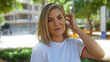 © Krakenimages.com - Woman brushing blonde hair with hand in urban park, showcasing vibrant city life and beauty outdoors on a sunny day.