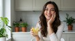 © Thierry - A happy woman holding a refreshing lemon drink in a glass, smiling and resting her hand on her cheek in a cozy kitchen with plants and natural light.