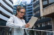 © Srdjan - Portrait of a successful business woman using digital tablet in front of modern business building. Businessperson office worker design professional occupation, innovative work outside of workspace.
