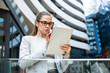 © Srdjan - Portrait of a successful business woman using digital tablet in front of modern business building. Businessperson office worker design professional occupation, innovative work outside of workspace.