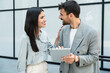 © Srdjan - Two businesspeople standing outside of modern office building using digital tablet working on new project discussing and explaining business matters and smiling. Design professional occupation persons