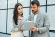 © Srdjan - Two businesspeople standing outside of modern office building using digital tablet working on new project discussing and explaining business matters and smiling. Design professional occupation persons