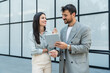 © Srdjan - Two businesspeople standing outside of modern office building using digital tablet working on new project discussing and explaining business matters and smiling. Design professional occupation persons