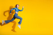 © deagreez - Young woman in stylish outfit joyfully jumping against a vibrant yellow background providing a cheerful and energizing atmosphere