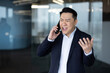 © Tetiana - Angry young Asian male businessman standing in the office and talking emotionally on the phone gesturing with his hands