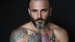 © danadesa - Shirtless tattooed man with a beard looking directly at the camera with an intense expression against a dark studio background.