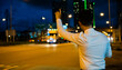 © sorapop - Man in suit hails taxi on city street at night. Woman smiles using phone app to call cab after late work. Urban transportation scene businessman gesturing for taxi.