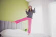 © deagreez - Cheerful Young Woman in Colorful Pajamas Jumping on Her Bed in a Bright Bedroom