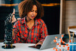© sorapop - Portrait of a Black teenage student in a classroom learning about a robotic arm for her engineering project. She skillfully controls the arm showcasing intelligence and innovation in technology.