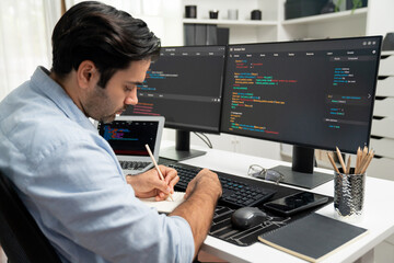 Smart IT developer writing data memo's software development on paper's coding on laptop and two pc screen, creating application program update version online website system at modern office. Surmise.