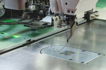 Poster - A sewing machine is in use, with a needle and thread being pulled through a piece of fabric. The machine is made of metal and has a green light on it