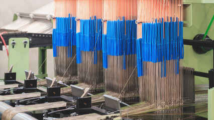 Poster - A machine is weaving a piece of fabric. The machine is made up of many parts, including a large metal piece that is connected to a hose