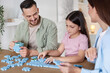 © New Africa - Happy parents and their daughter solving puzzle together at wooden table indoors