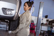 © Wavebreak Media - Female mechanic inspecting car tire in garage, focusing on maintenance work