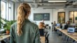 © STK - Woman with blonde ponytail in green jacket walks through modern office, looking towards a blurred background of coworkers at desks and computers. Natural lighting.