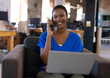 © Wavebreak Media - Smiling woman in blue shirt using laptop and talking on phone at office