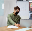 © wavebreak3 - Asian man wearing mask using laptop in office, analyzing business charts