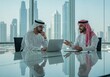© Poetra RH - Two Middle Eastern businessmen in traditional attire discuss ideas in a modern office with a city skyline view. One gestures while speaking, the other listens thoughtfully, working on a laptop.