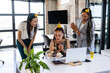 © Wavebreak Media - Celebrating birthday in office, diverse female colleagues wearing party hats and sharing cupcakes