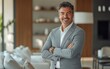 © Fathor - Editorial eye-level, waist-up shot of a man in his forties, wearing a grey suit, arms crossed and smiling, looking at the camera, standing against a modern living room. Realistic photography style,
