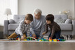 © fizkes - Creative playtime with grandpa. Happy family old grandfather two grandkids brothers preschoolers enjoy playing with toys on warm floor in living room creating fantasy city using building blocks cars