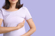 © Pixel-Shot - Young woman checking her breast on lilac background, closeup. Cancer awareness concept