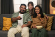 © pressmaster - Family enjoying time relaxing on couch while sharing popcorn and smiling. Daughter hugging her parents, showing happiness in comfortable living space