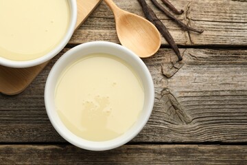 Wall Mural - tasty condensed milk, spoon and vanilla pods on wooden table, flat lay. space for text