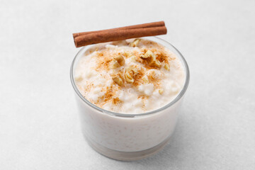 Wall Mural - tasty rice pudding with cinnamon and nuts in glass bowl on light grey table, closeup