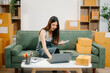 © Nuttapong punna - Young business owner woman prepare parcel box and standing check online orders for deliver