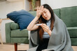© Nuttapong punna - Young Asian woman suffering from flu symptoms, covered with a blanket on a sofa. Concept of illness, healthcare,